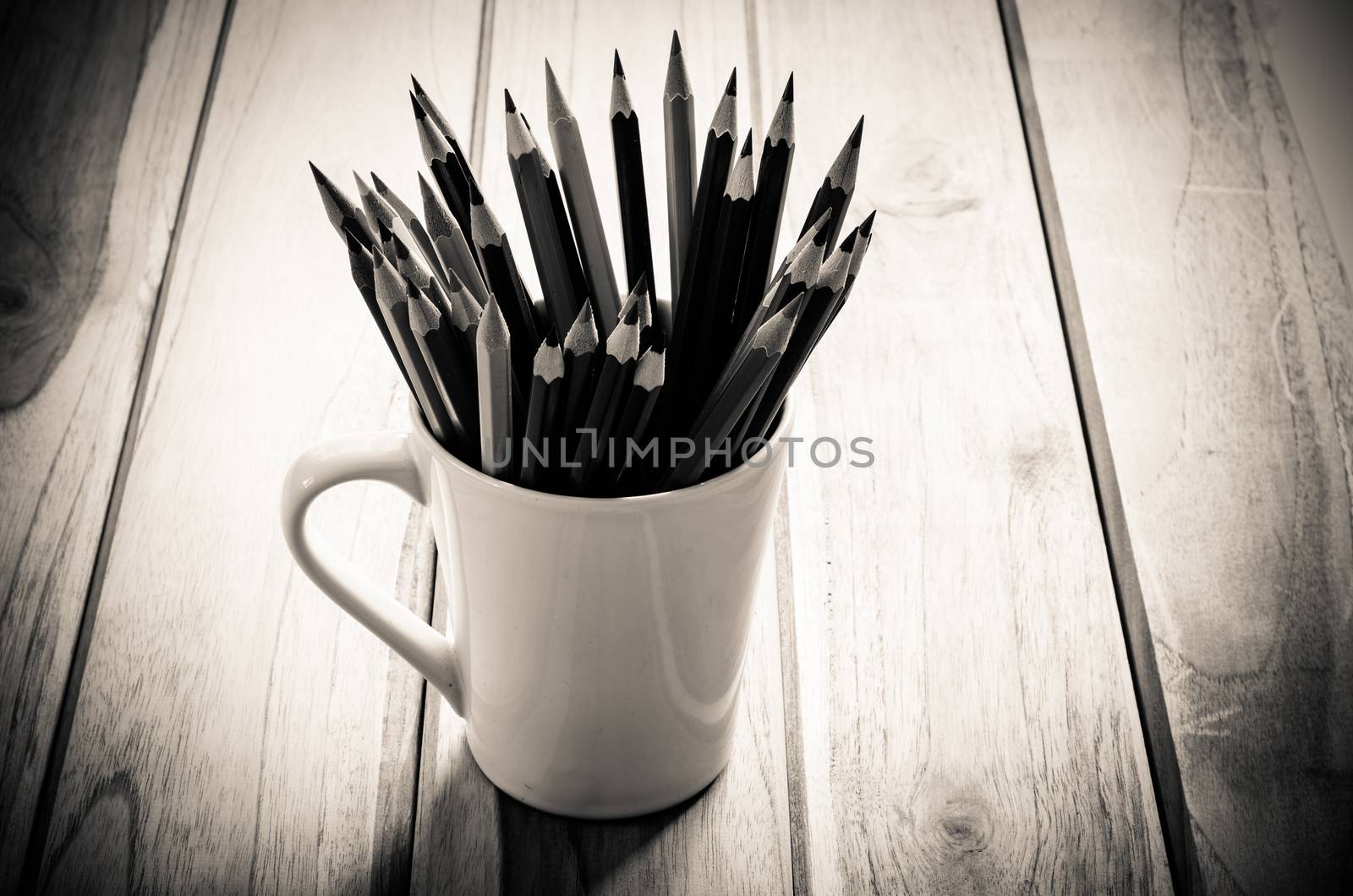 Stack of pencils in a glass on wooden background,tone sepia by photobyphotoboy