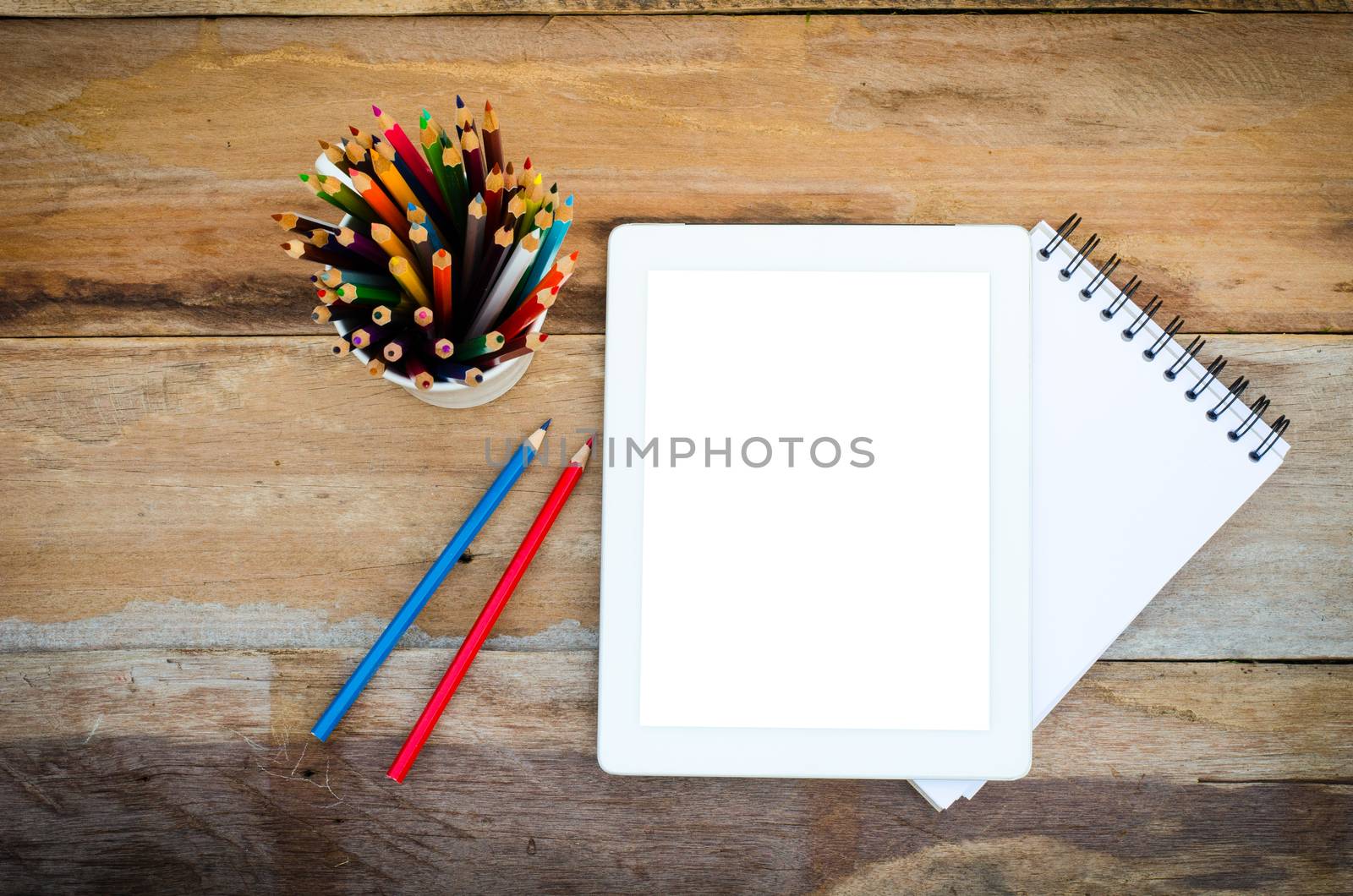 Color pencils in the cups and notebook placed on a desk. by photobyphotoboy