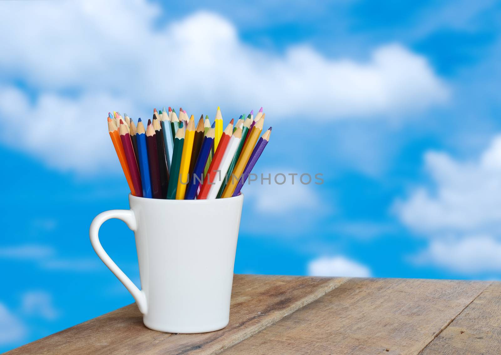 colored pencils in a glass on wooden background clouds in the sky