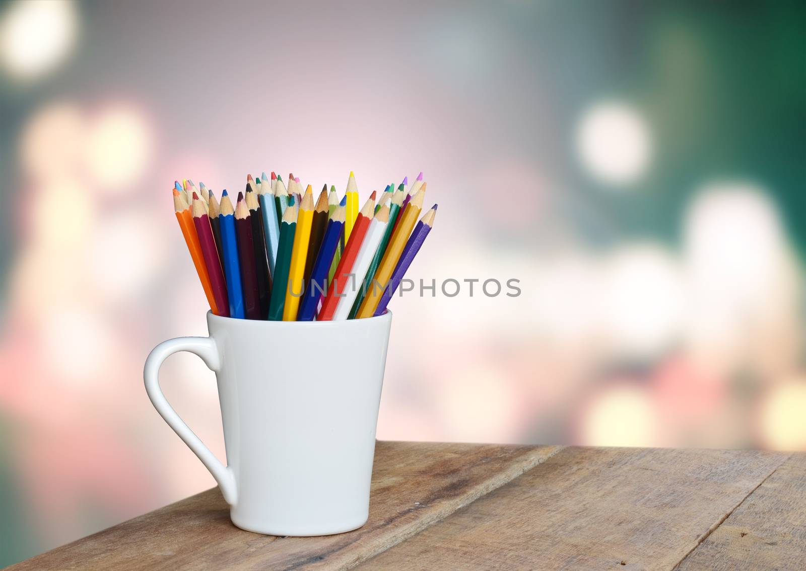 colored pencils in a glass on wooden background light bokeh