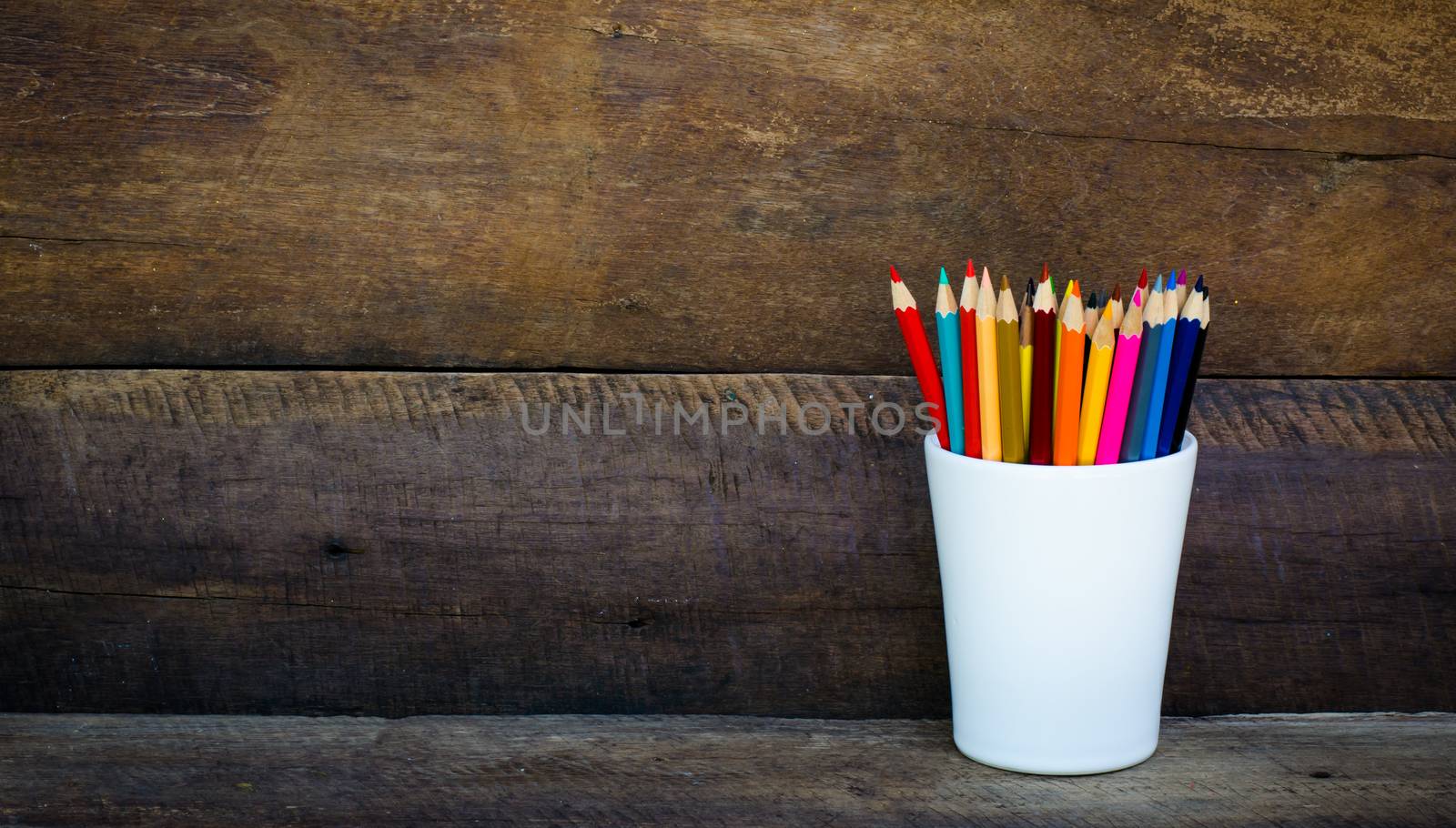 Stack of colored pencils in a glass on wooden background by photobyphotoboy