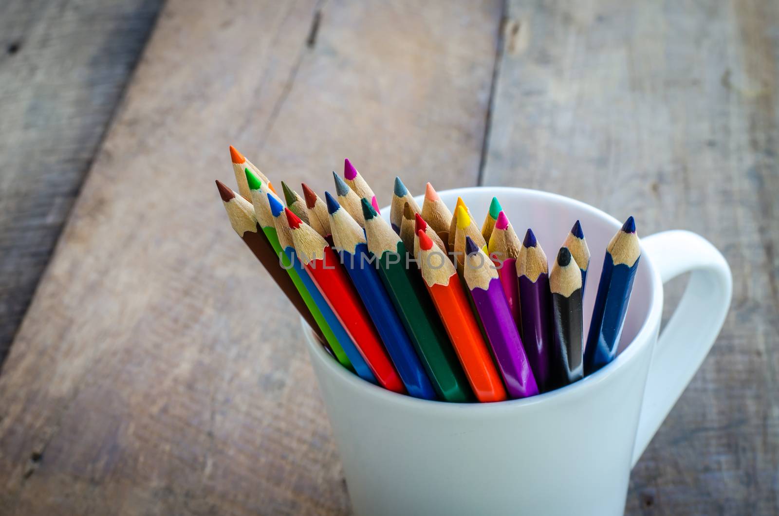 Stack of colored pencils in a glass on wooden background