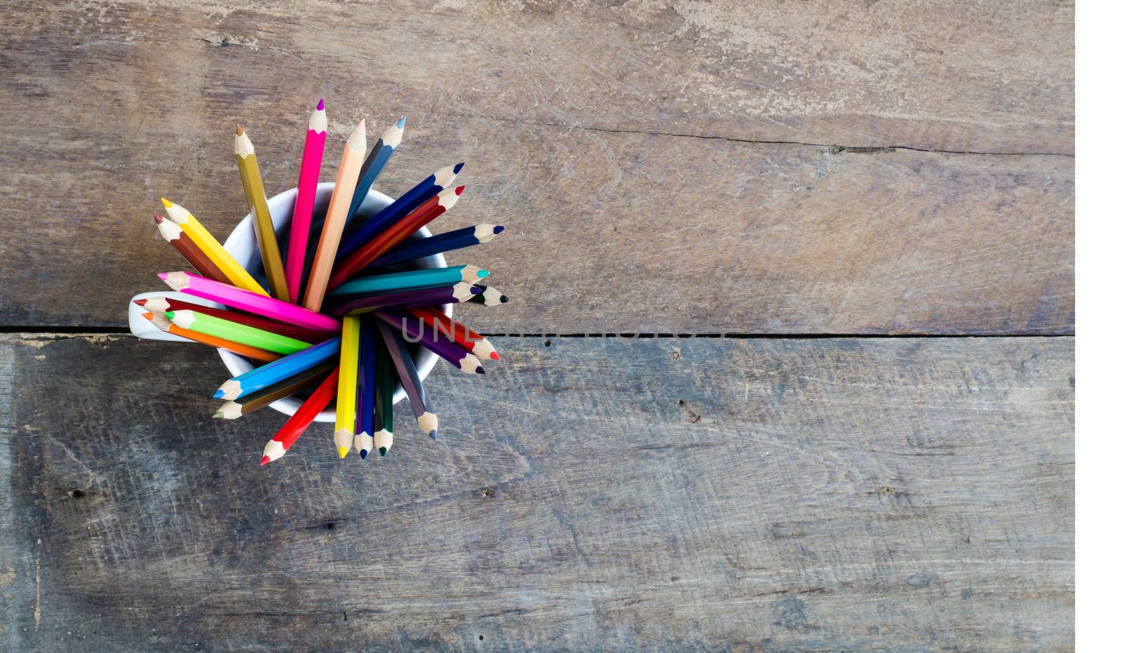 Stack of colored pencils in a glass on wooden background