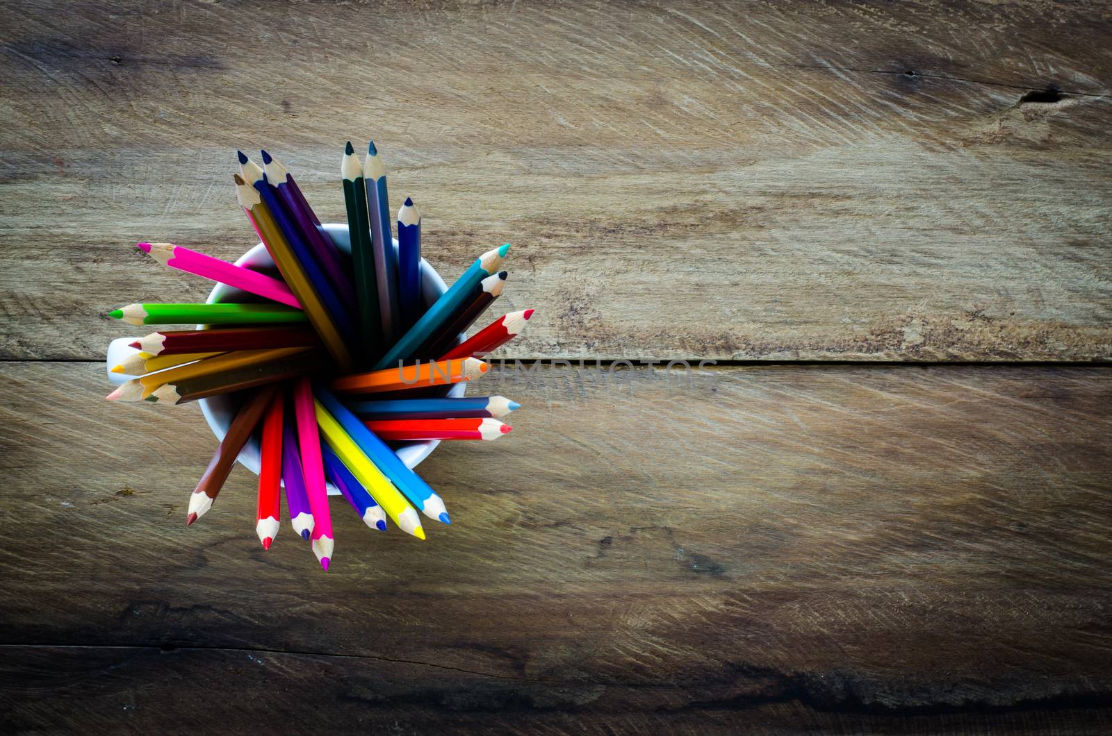 Stack of colored pencils in a glass on wooden background