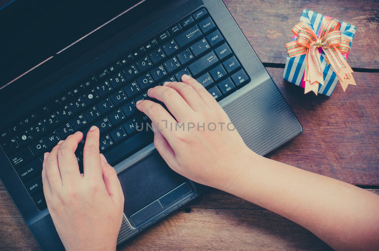 hands typing on laptop and gift on wooden background