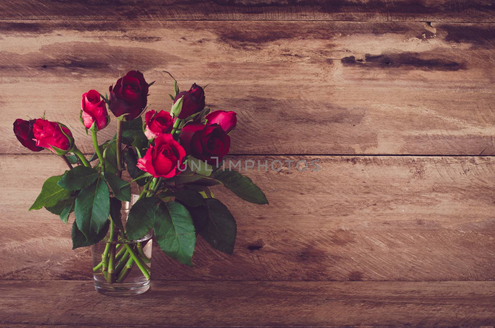 Red roses in glass on wooden background. by photobyphotoboy