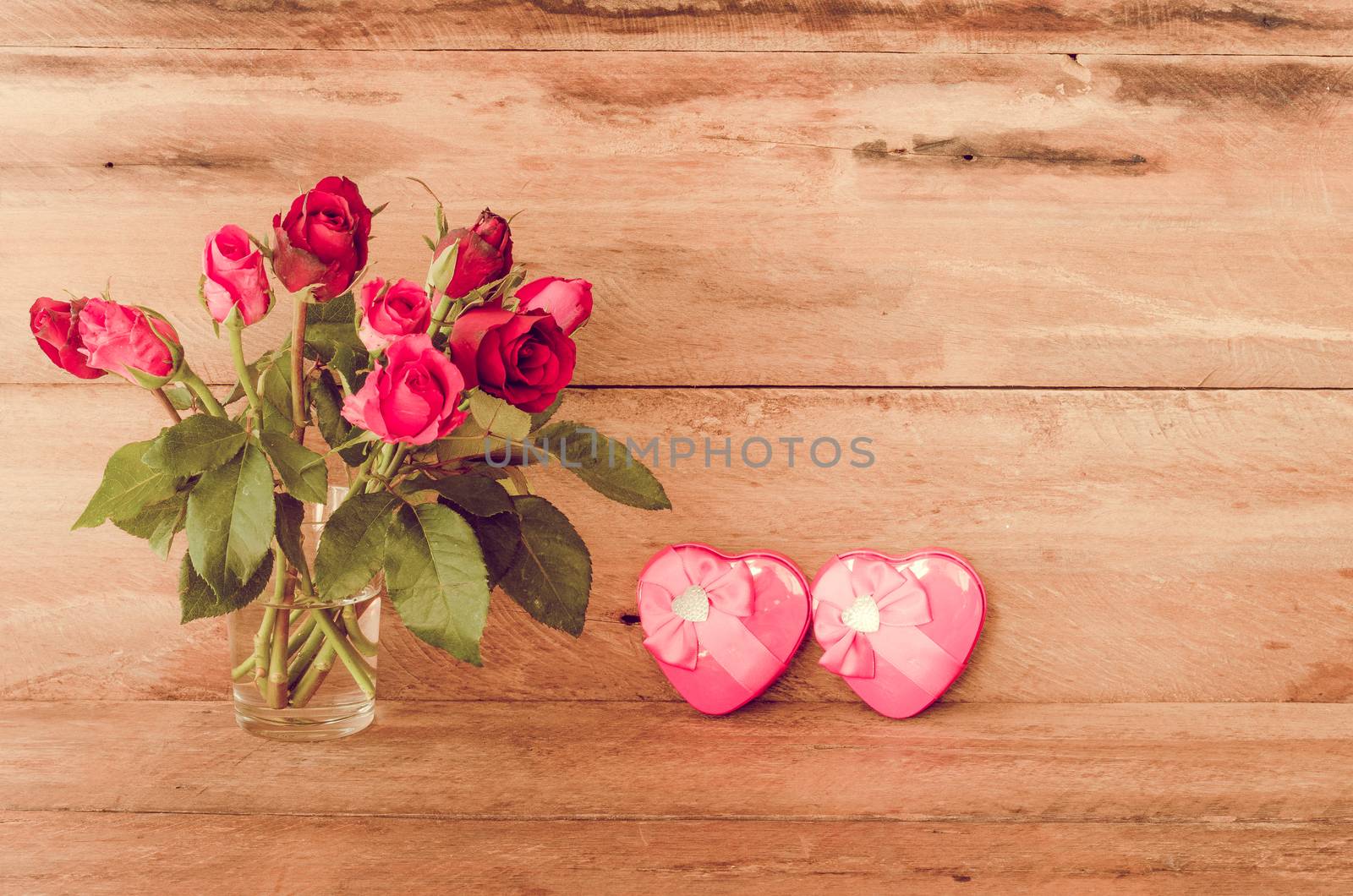Red roses in glass and Heart shaped Valentine's Day gift box on wooden background.