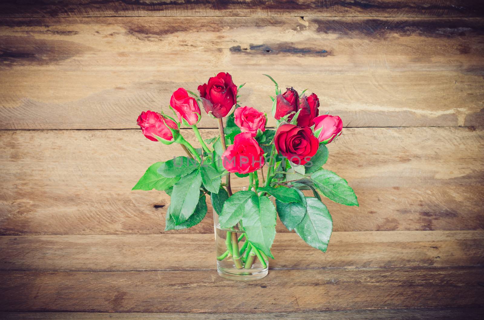 red roses in glass on wooden bacgrould