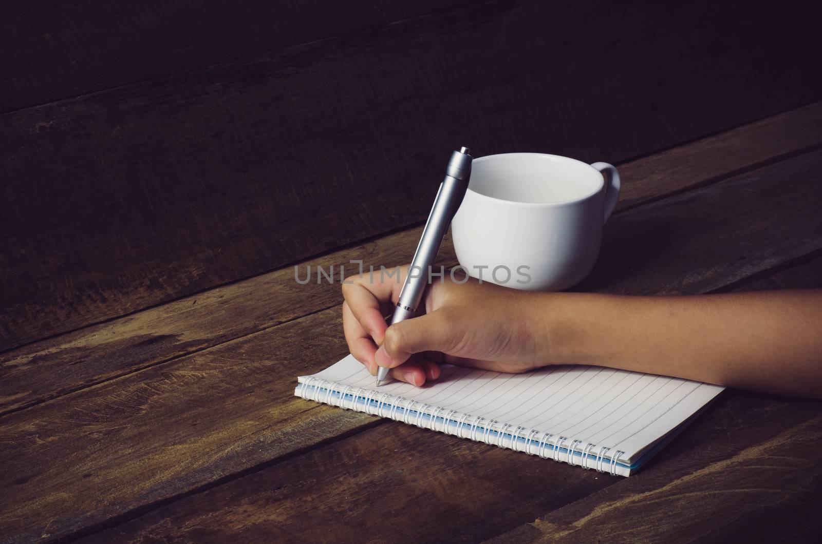 Hand writing in open notebook on table by photobyphotoboy