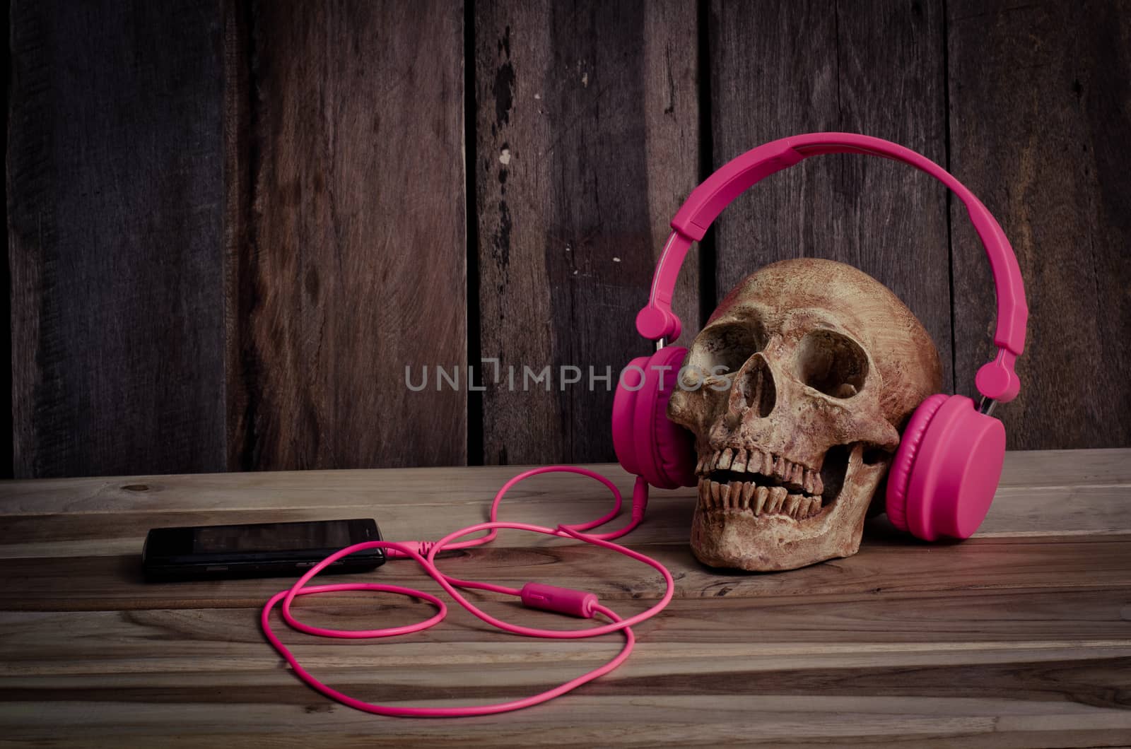 Still life human skull model with pink headphones on wooden background