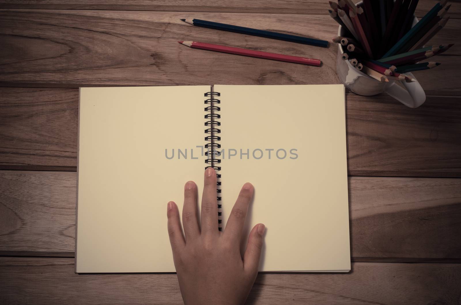 hand and a notebook on a wooden table. by photobyphotoboy