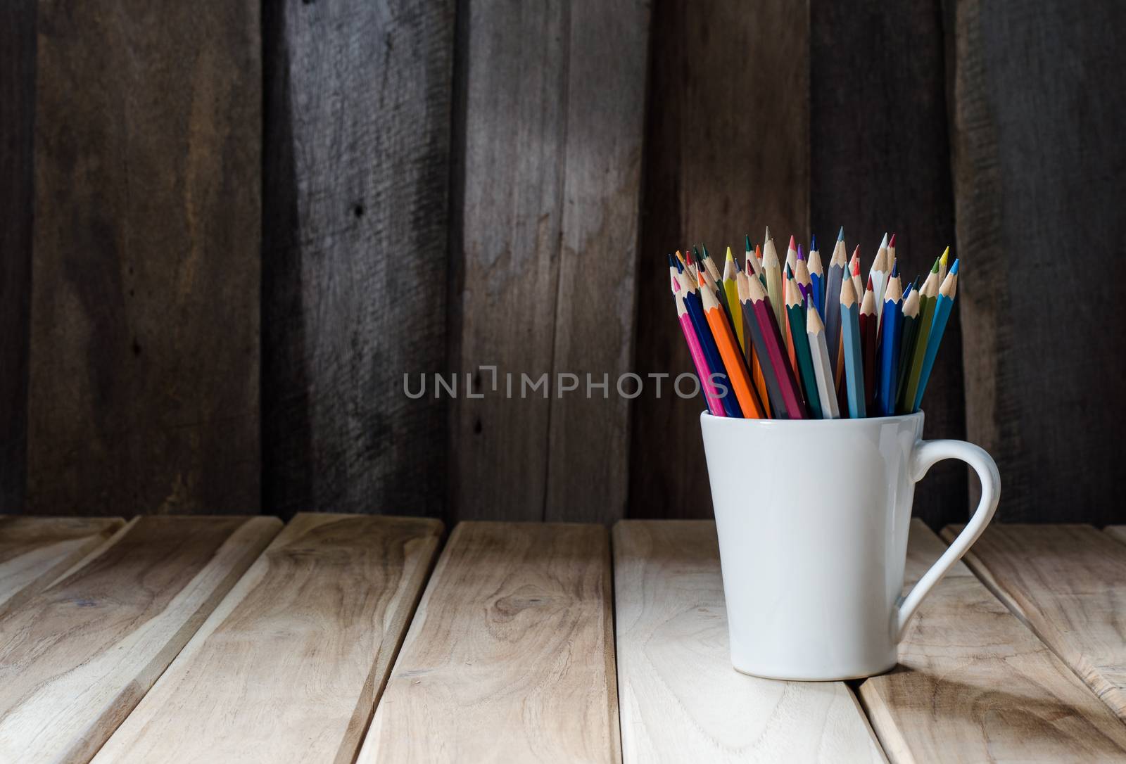 Stack of colored pencils in a glass on wooden background