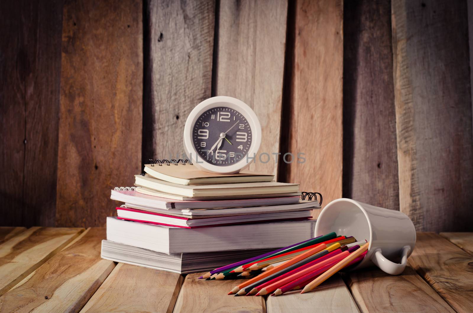 Crayons stack of books and clock on desk a wooden floor.