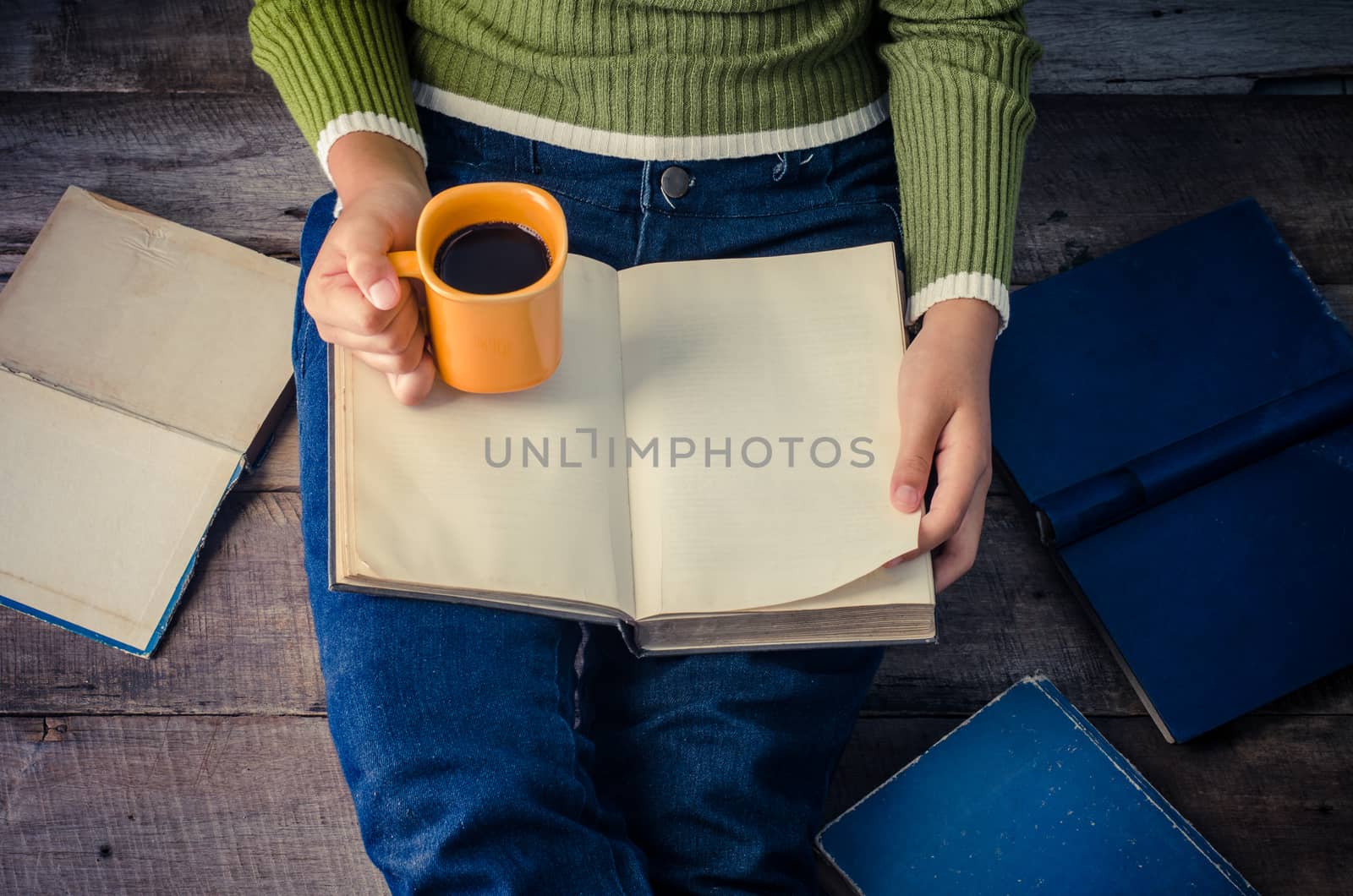 woman is sitting on a wooden floor and reading a book while holding a coffee cup