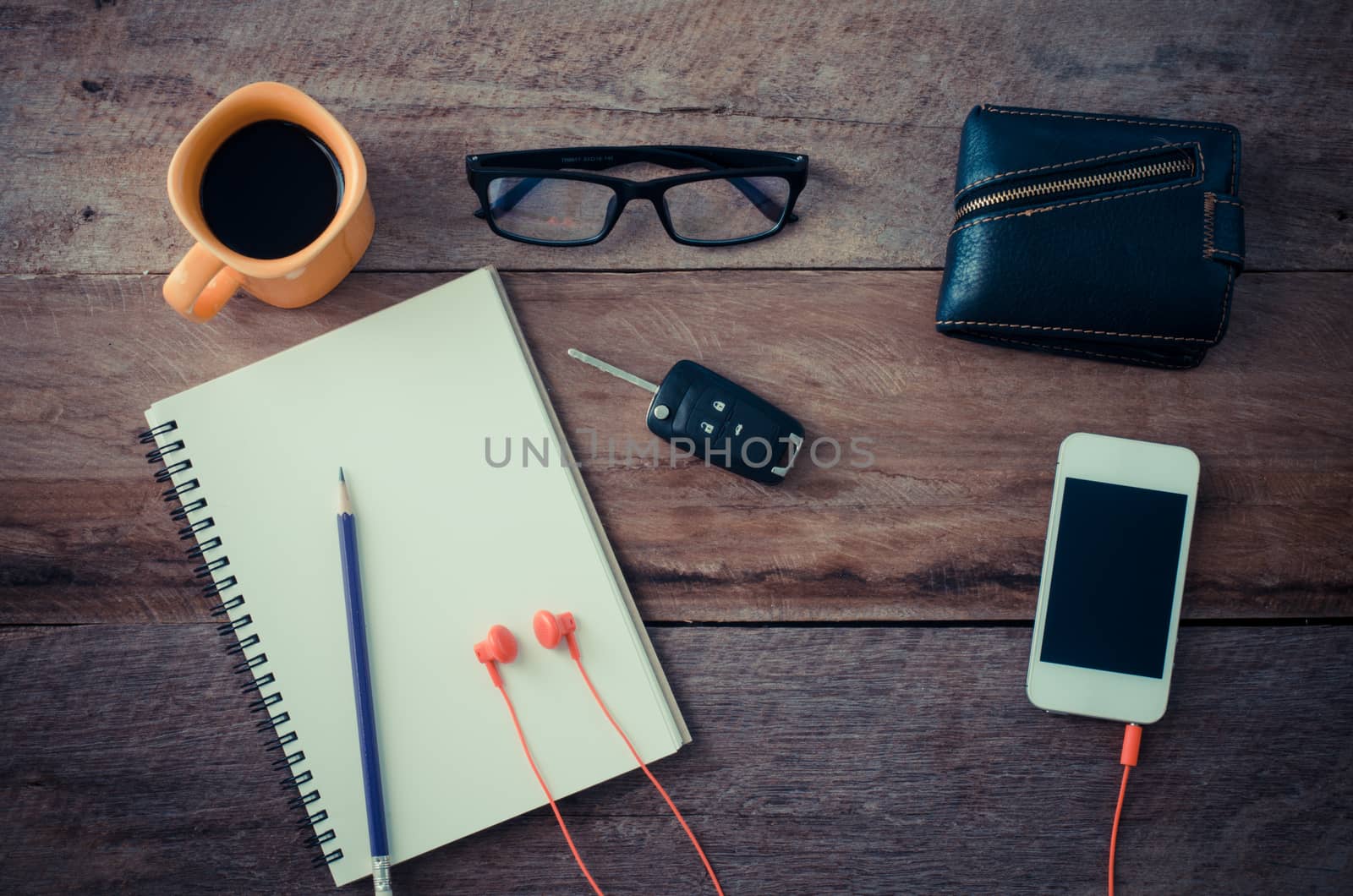 The surface of a wooden table with a notebook, smart-phone, glasses, wallet, car keys, coffee cup