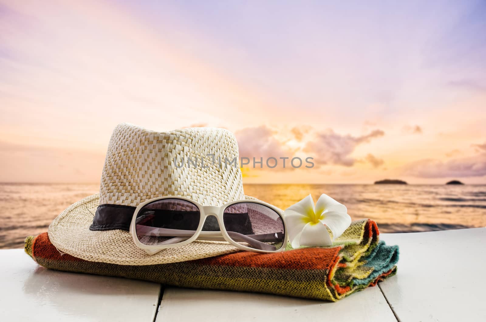 Hats, glasses, scarves, flowers are placed on a wooden floor with the sea as background.