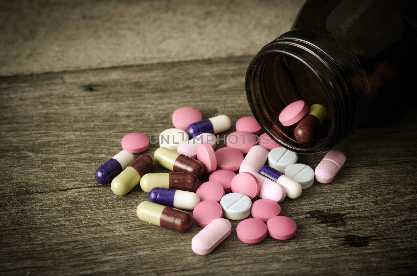 Different types of pills lying on a wooden floor.