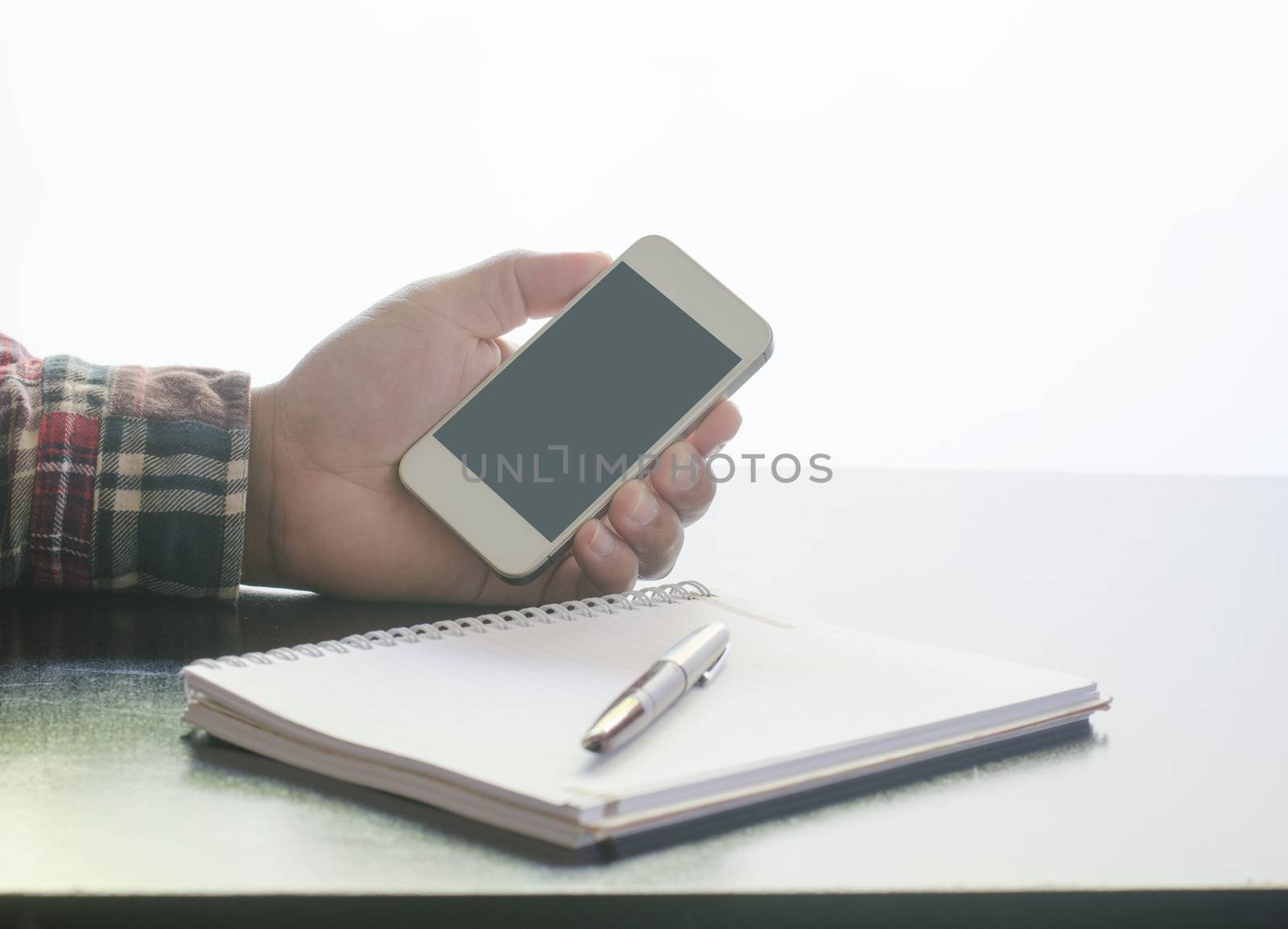Business man holding smartphone and notebook pen on the wood