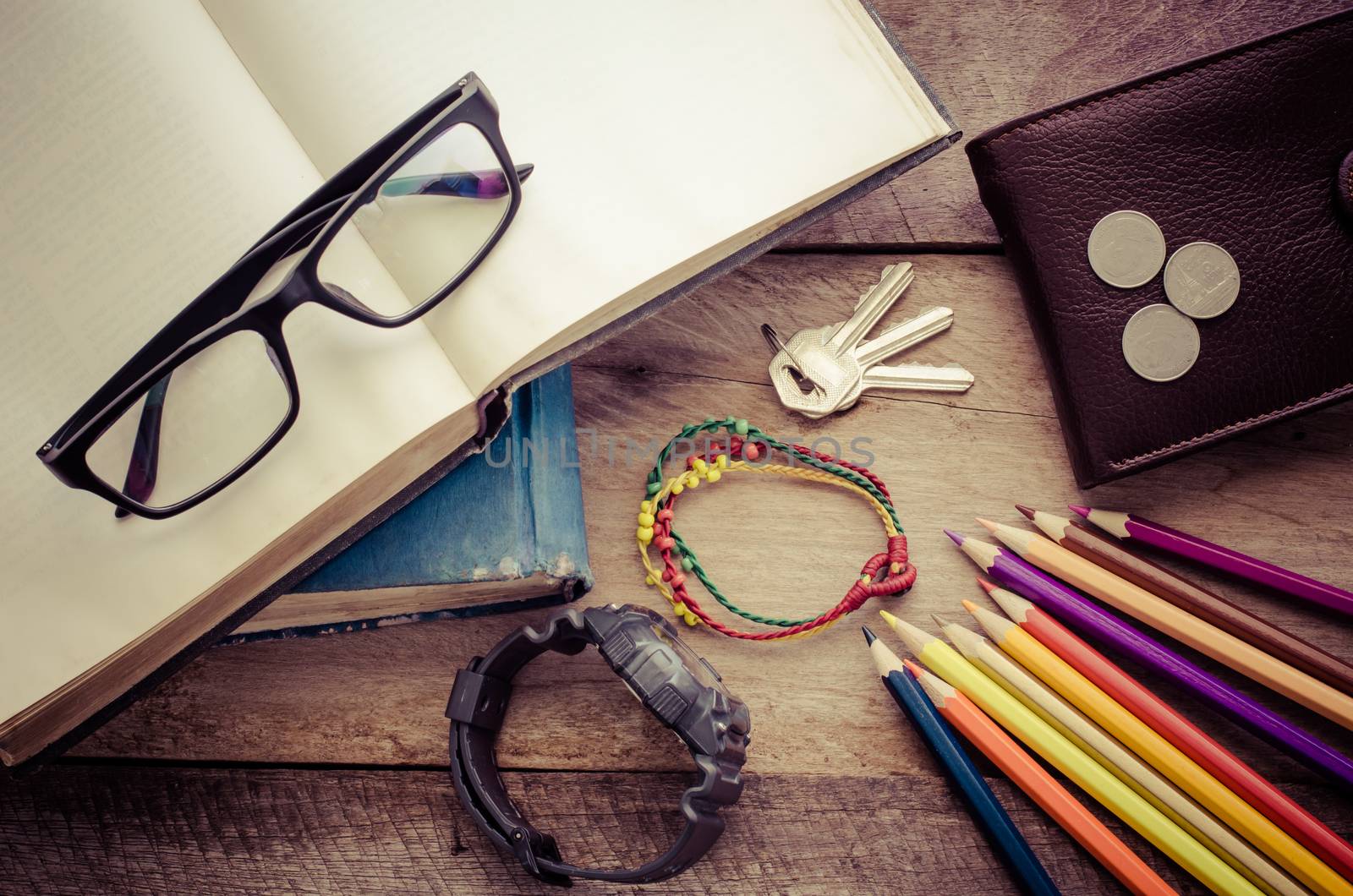 Equipment notebooks, colored pencils, watches, glasses, wallet, coins placed on a wooden floor.