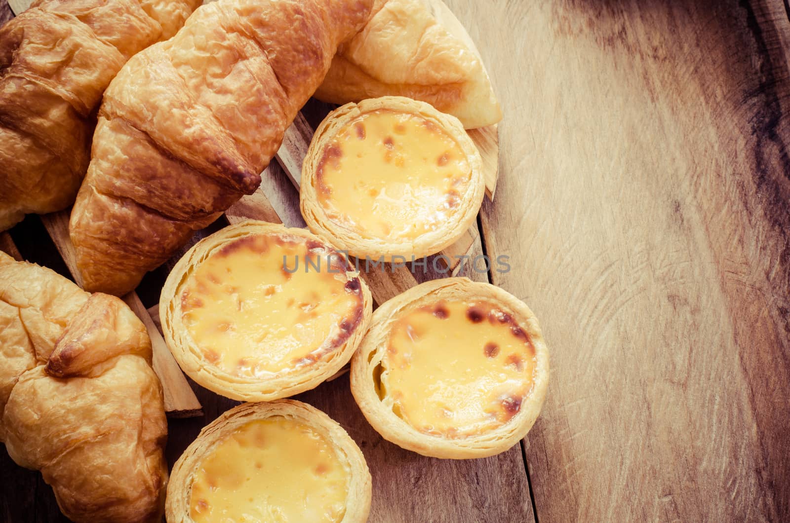 Egg tarts and croissants on a wooden table - tone vintage