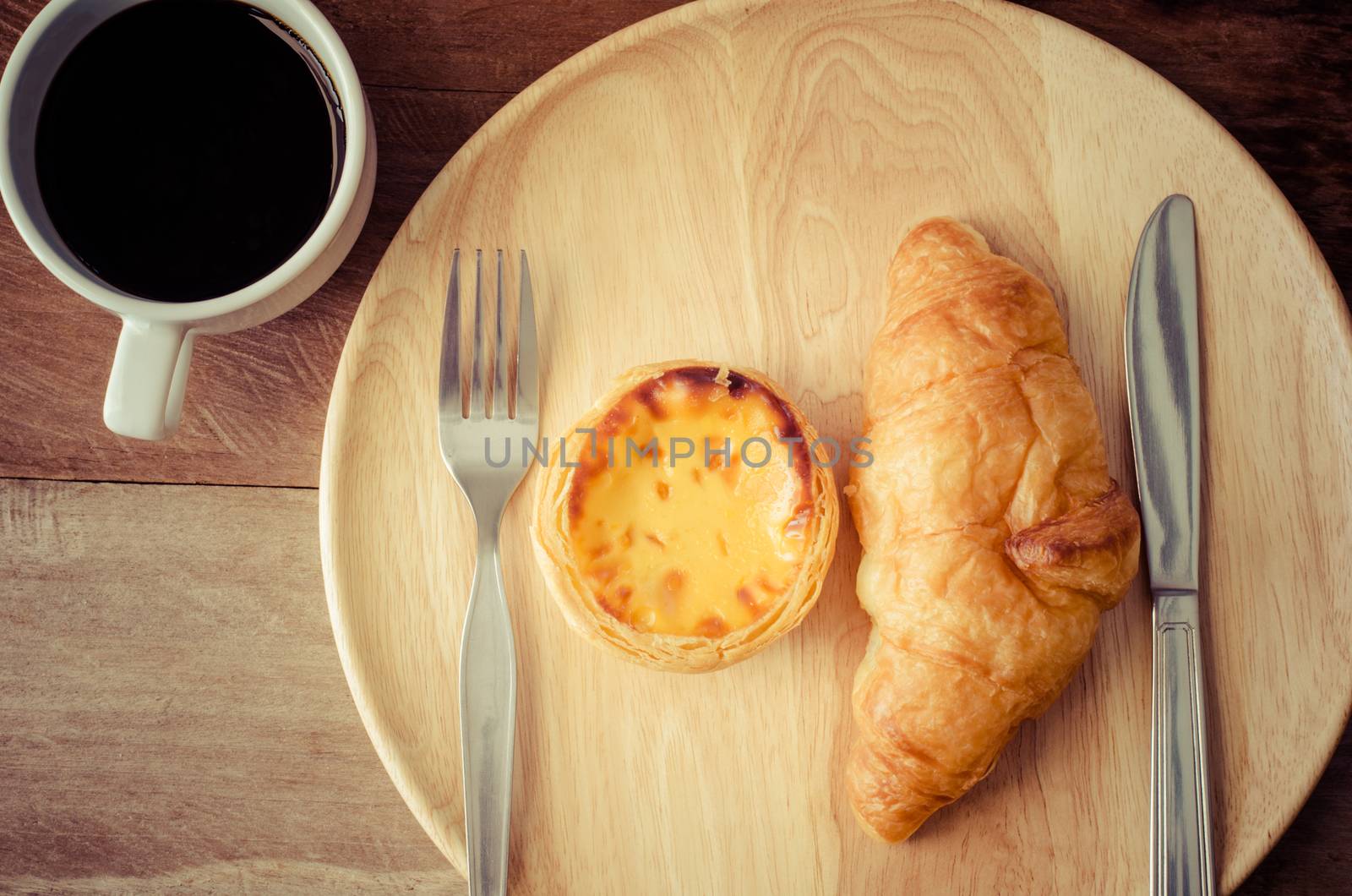 Croissants egg tart spoon and knife, cup coffee on the wooden table - tone vintage