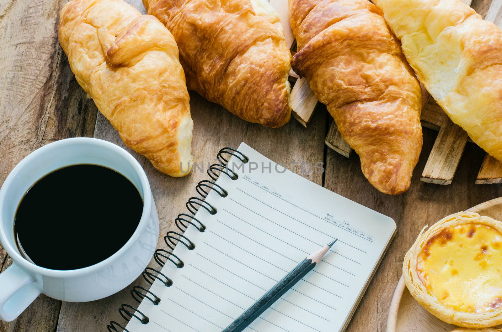 Croissants coffee notebook and pencil on the wooden table - tone vintage