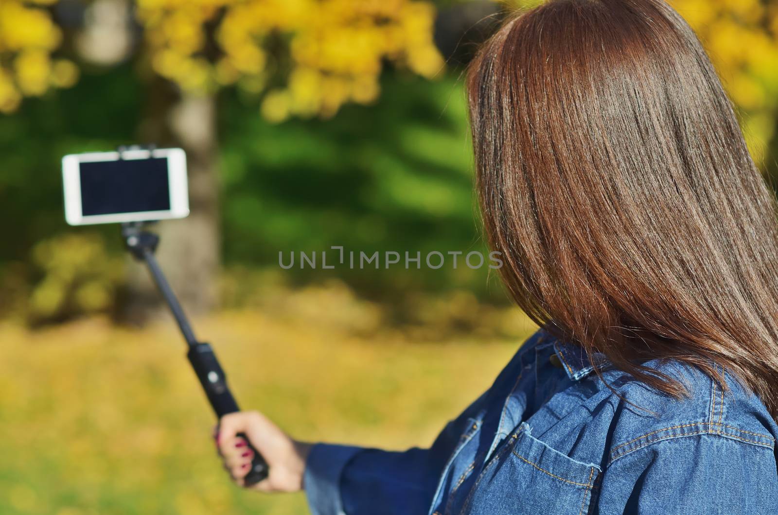 A young beautiful girl in a denim suit looks at the phone and takes a selfie walking in the city Park in the autumn, horizontal photo