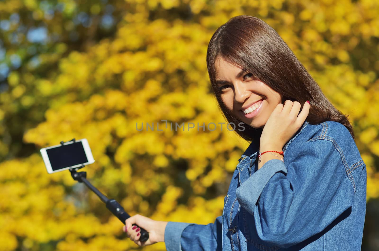 A young beautiful girl student in a denim suit looks at the camera and takes a selfie walking in the city Park in the autumn, horizontal photo