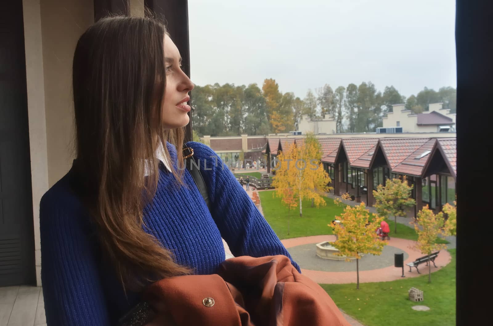 European girl looks at the window on the trees and the building