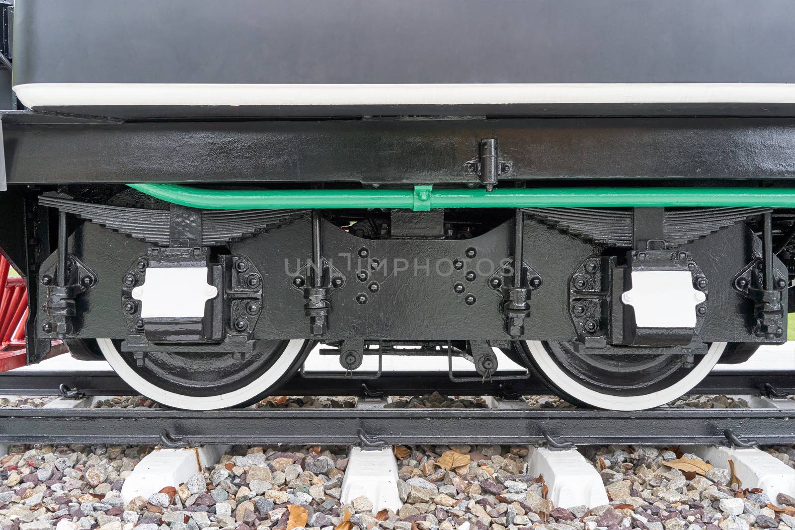 Black and white wheel of train with shock absorber and green pipe with railway on rocky.