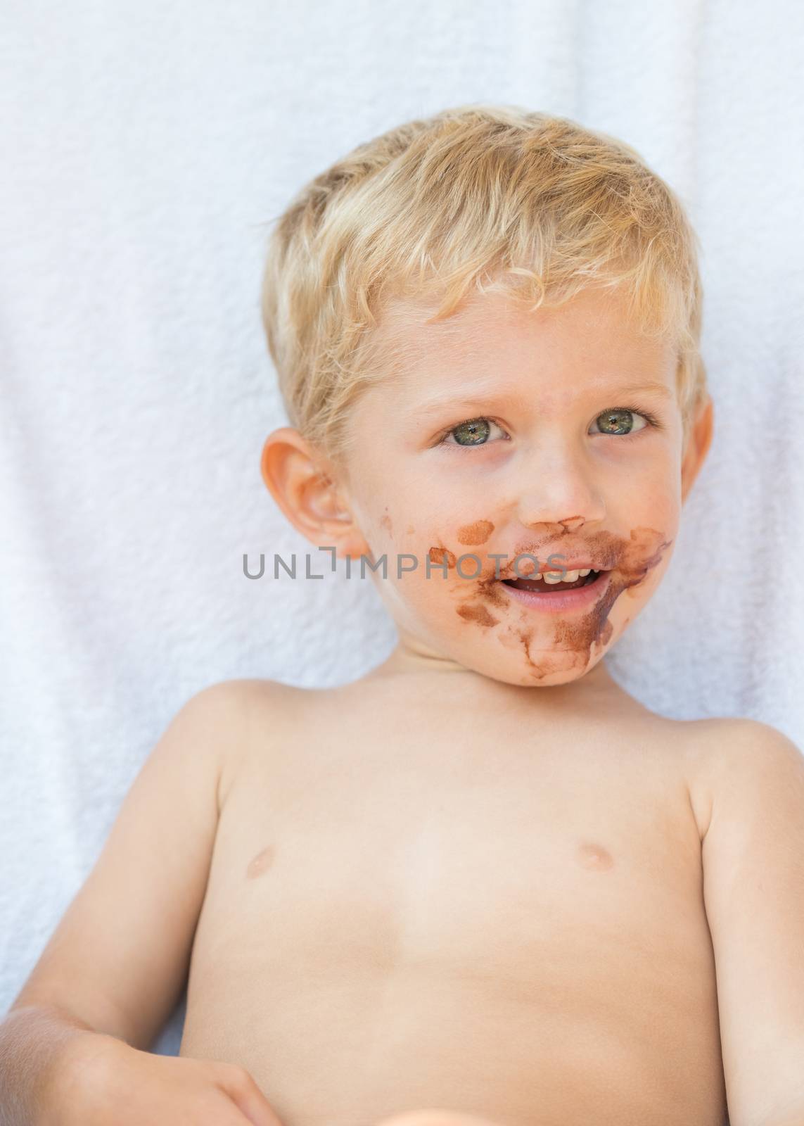 Portrait of fair-haired baby boy with chocolate on his face isolated on white background.