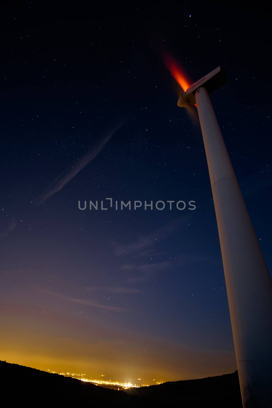 Wind turbine at night with city lights by mikelju