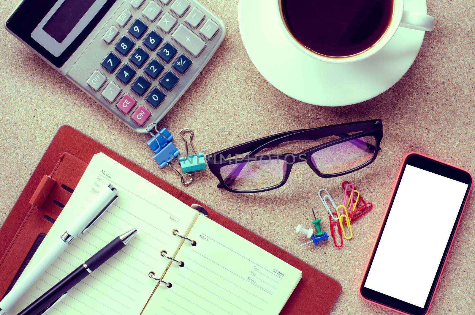 A cup coffee smart phone and office supplies on the table