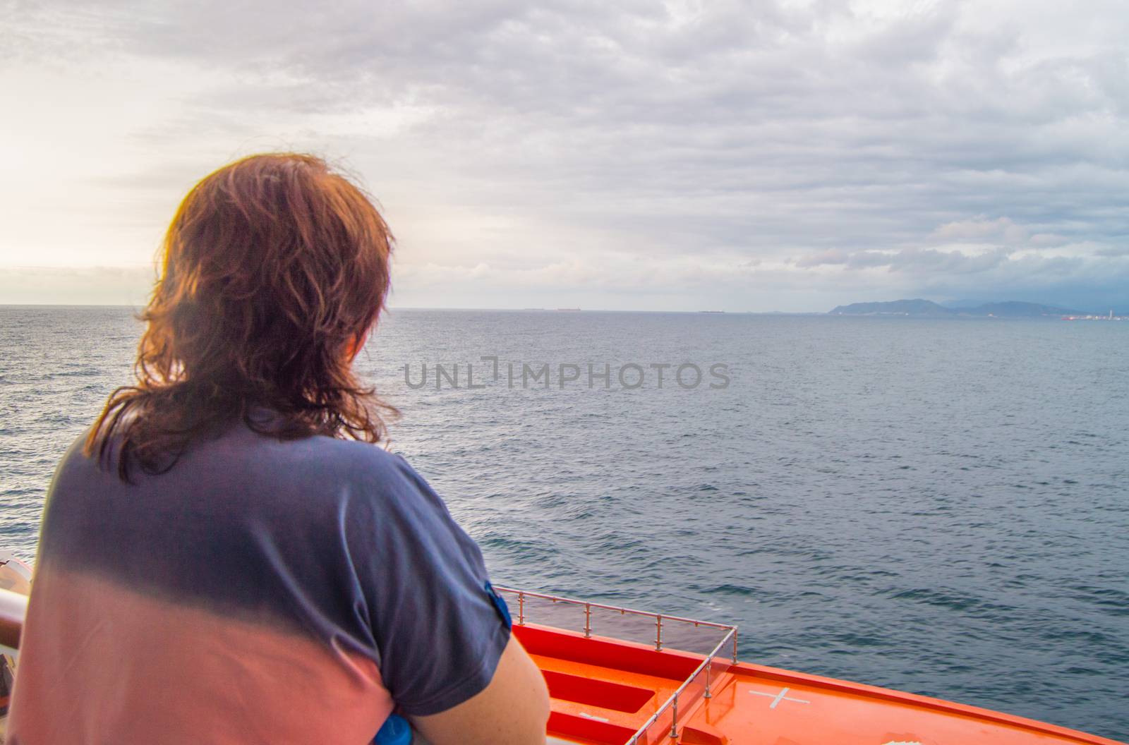 Happy woman looking at the coastline and the sea, enjoying the cruise ship journey, the view from the back.