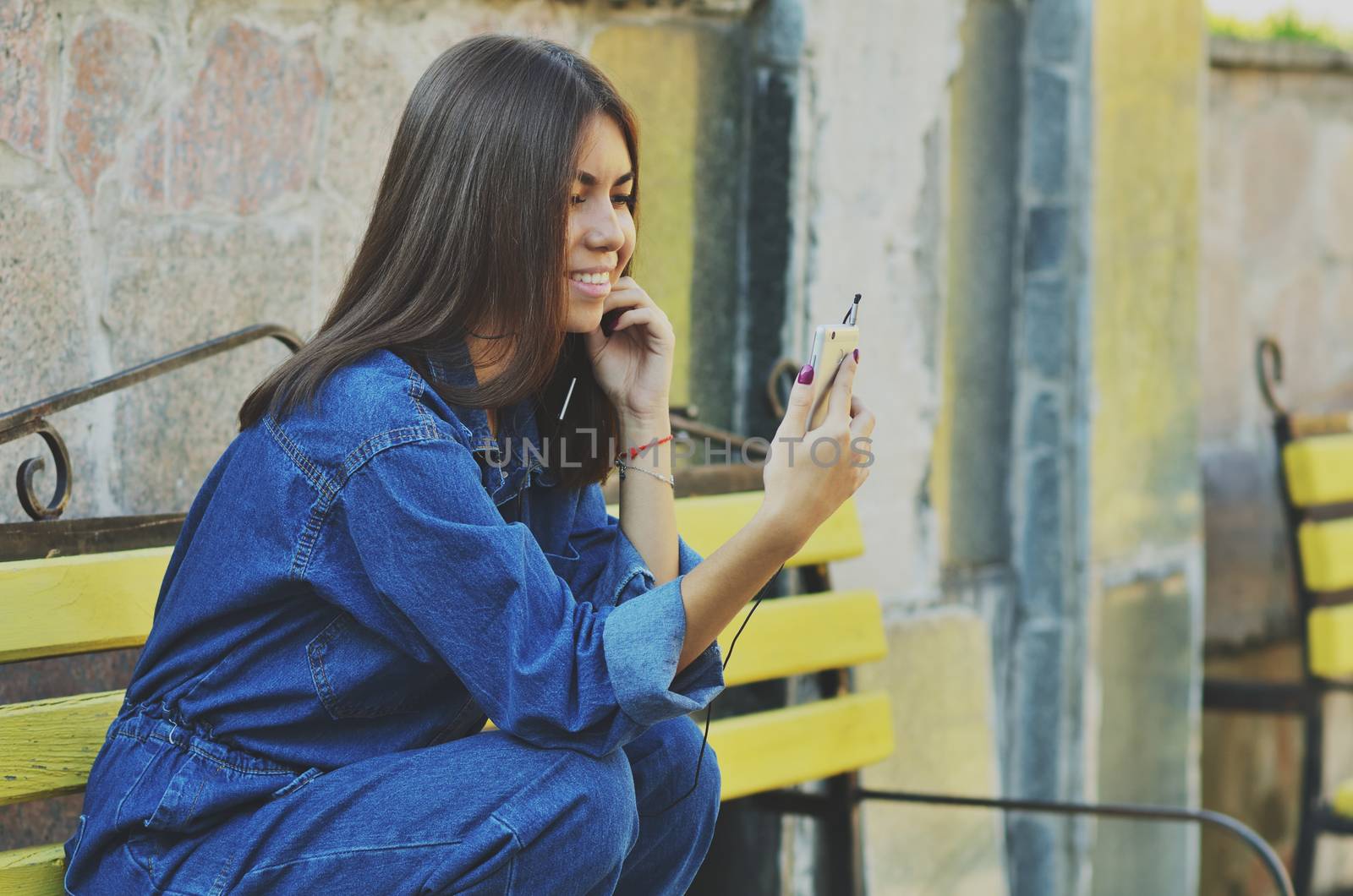 Young beautiful Asian girl sitting on a bench talking on the phone, horizontal photo, campus