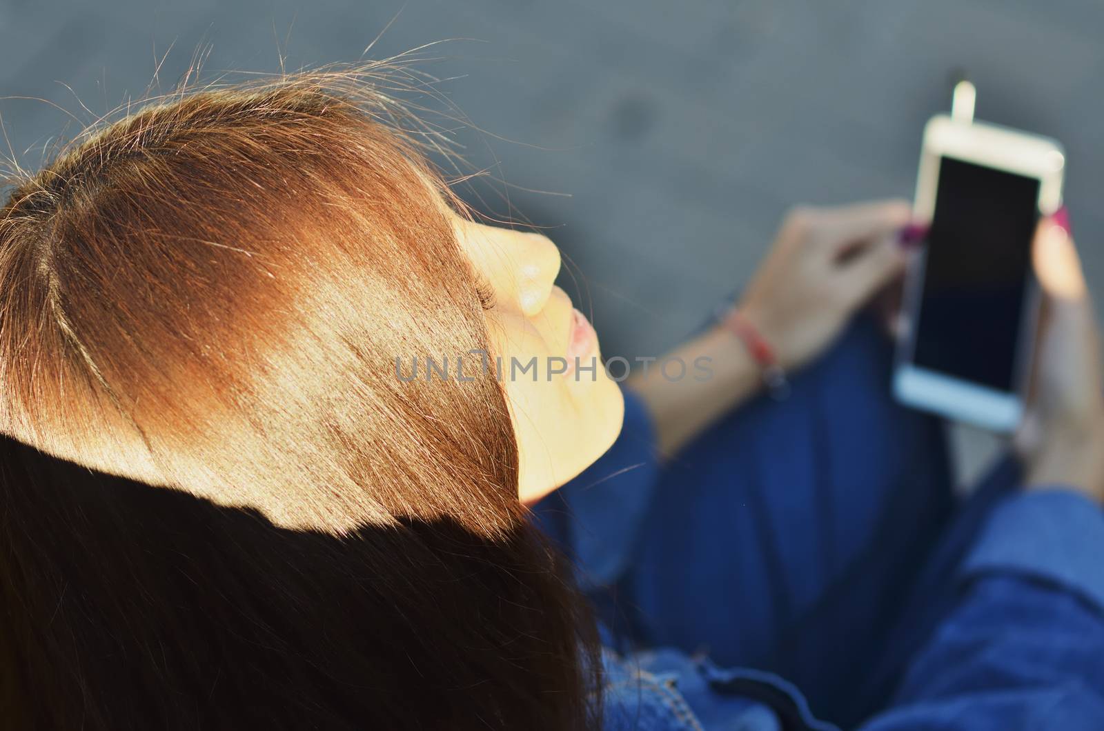 Portrait of a young attractive girl dressed in denim clothes who enjoys listening to music outside in the Park