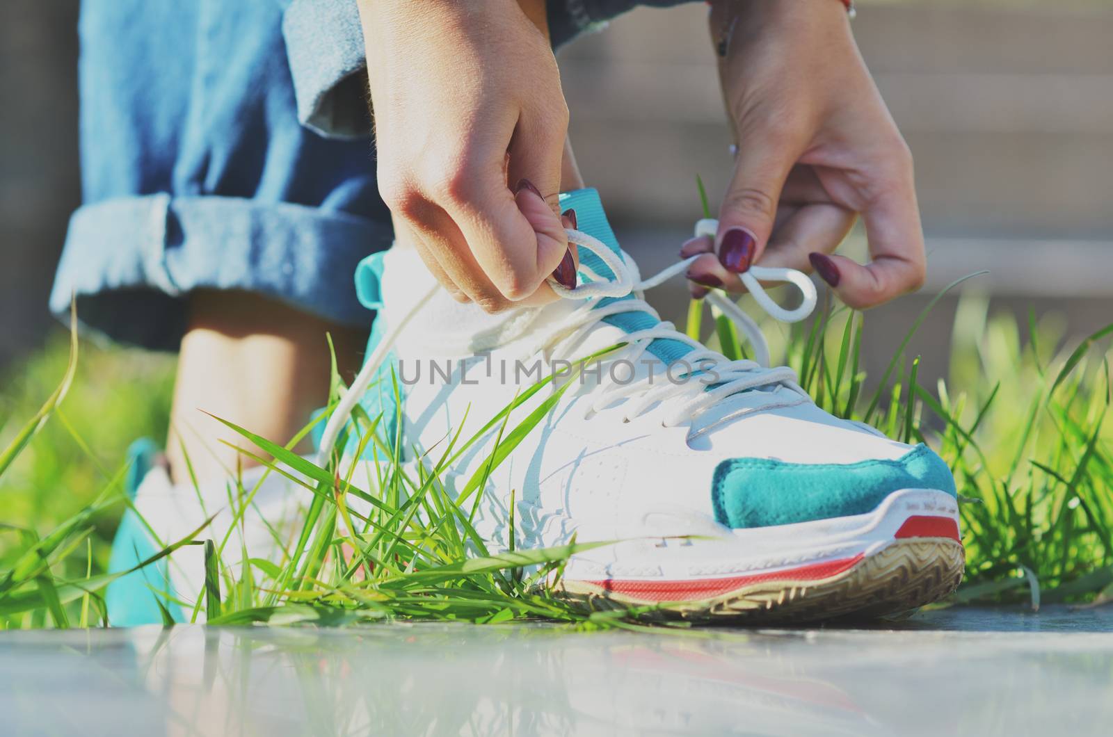 Young girl wearing jeans tying shoelaces on sneakers standing on green grass side view close-up horizontal photo, Sunny day