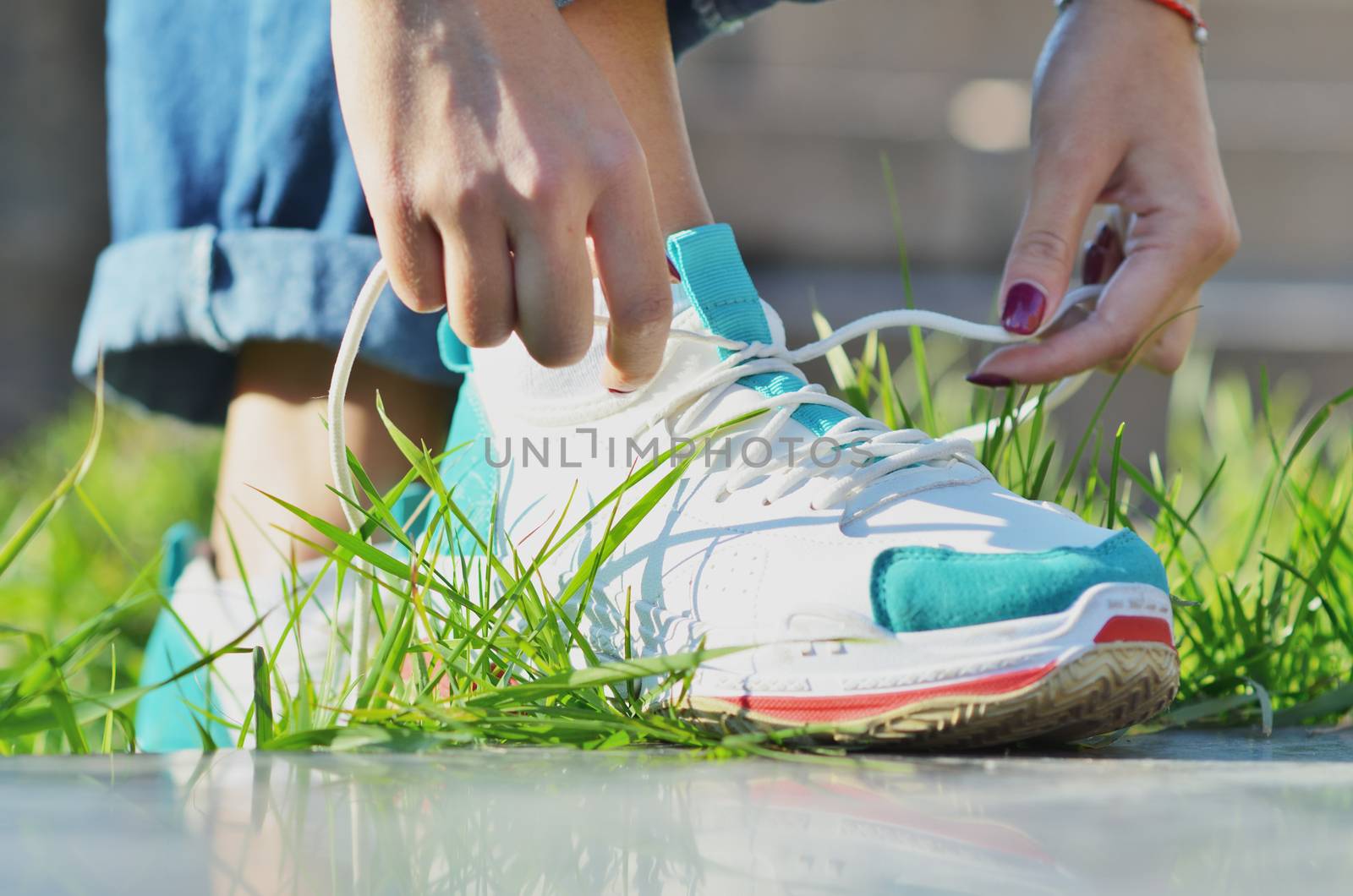 Young girl wearing jeans tying shoelaces on sneakers standing on green grass side view close-up horizontal photo, Sunny day