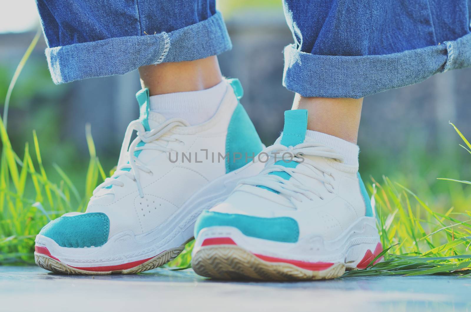 Girl in sneakers standing near the green grass on a Sunny day, side view