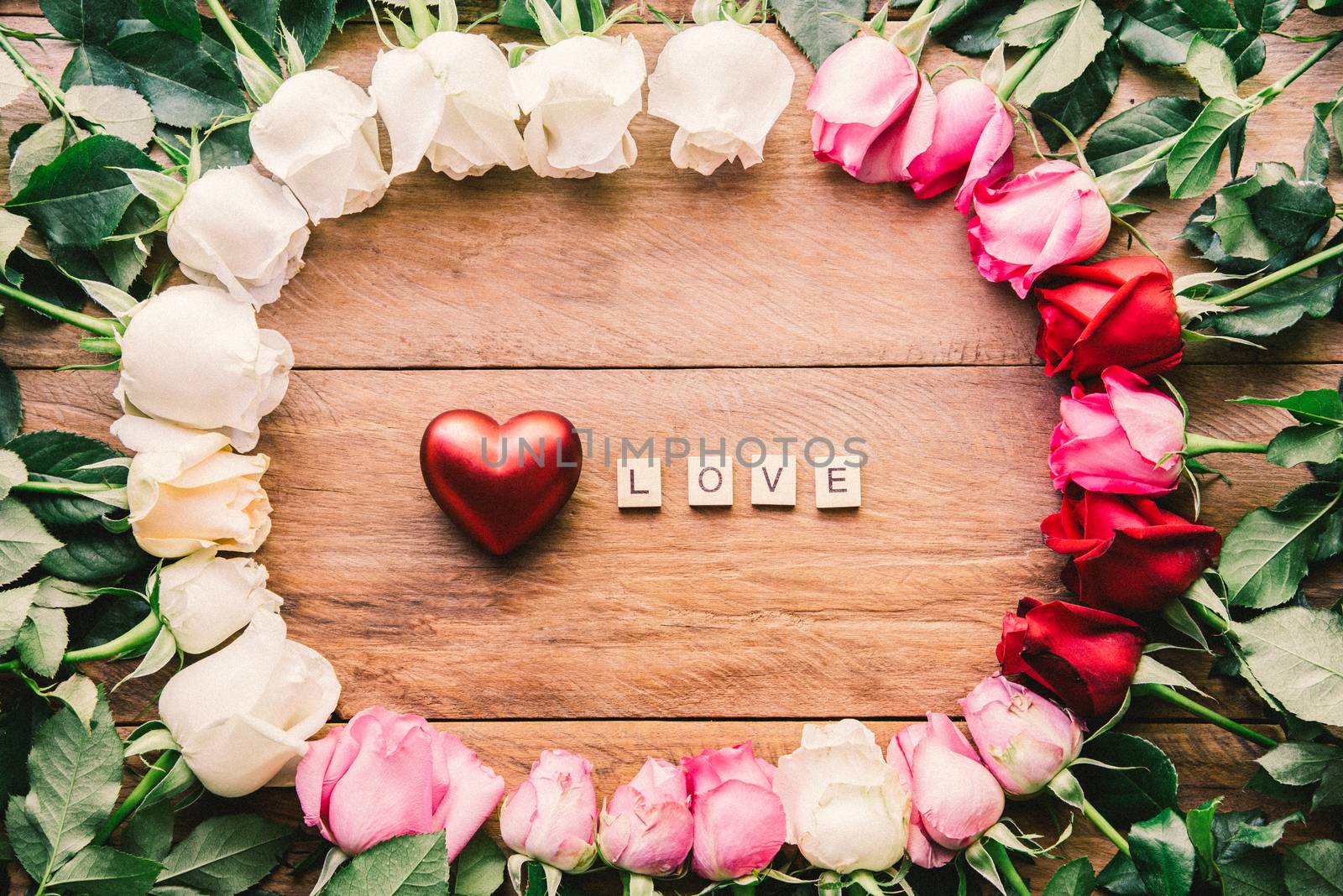 Colorful roses lined up on a wooden floor with heart and word "LOVE" - concept for love