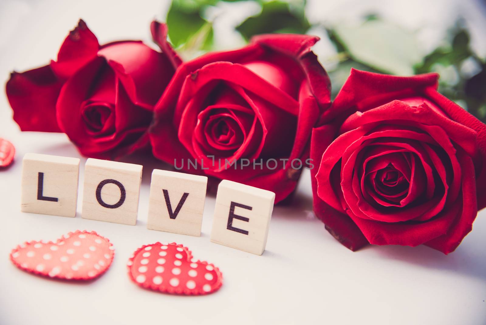 The red roses are placed on a white background and the wooden letters lined the word "love".