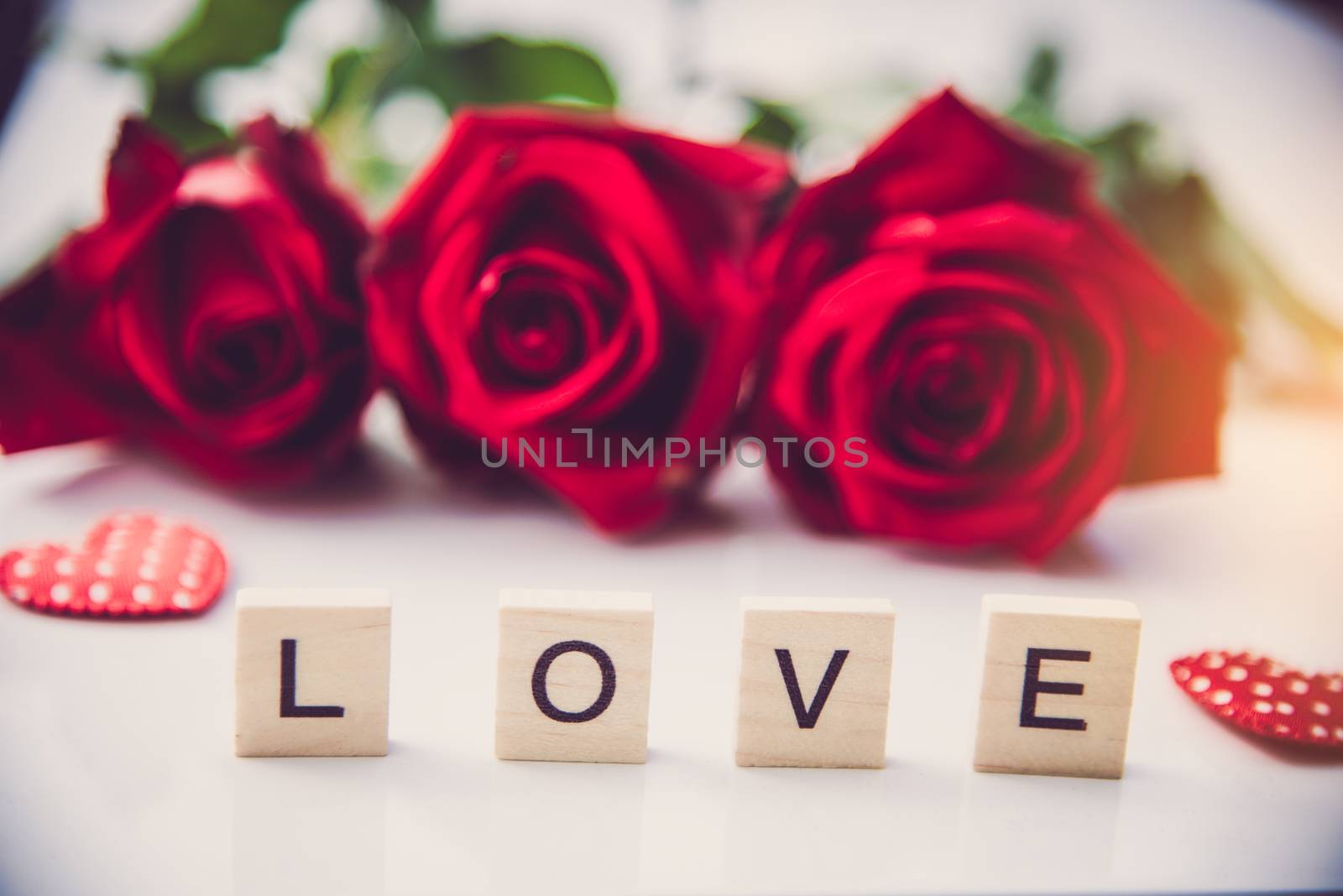 The red roses are placed on a white background and the wooden letters lined the word "love".