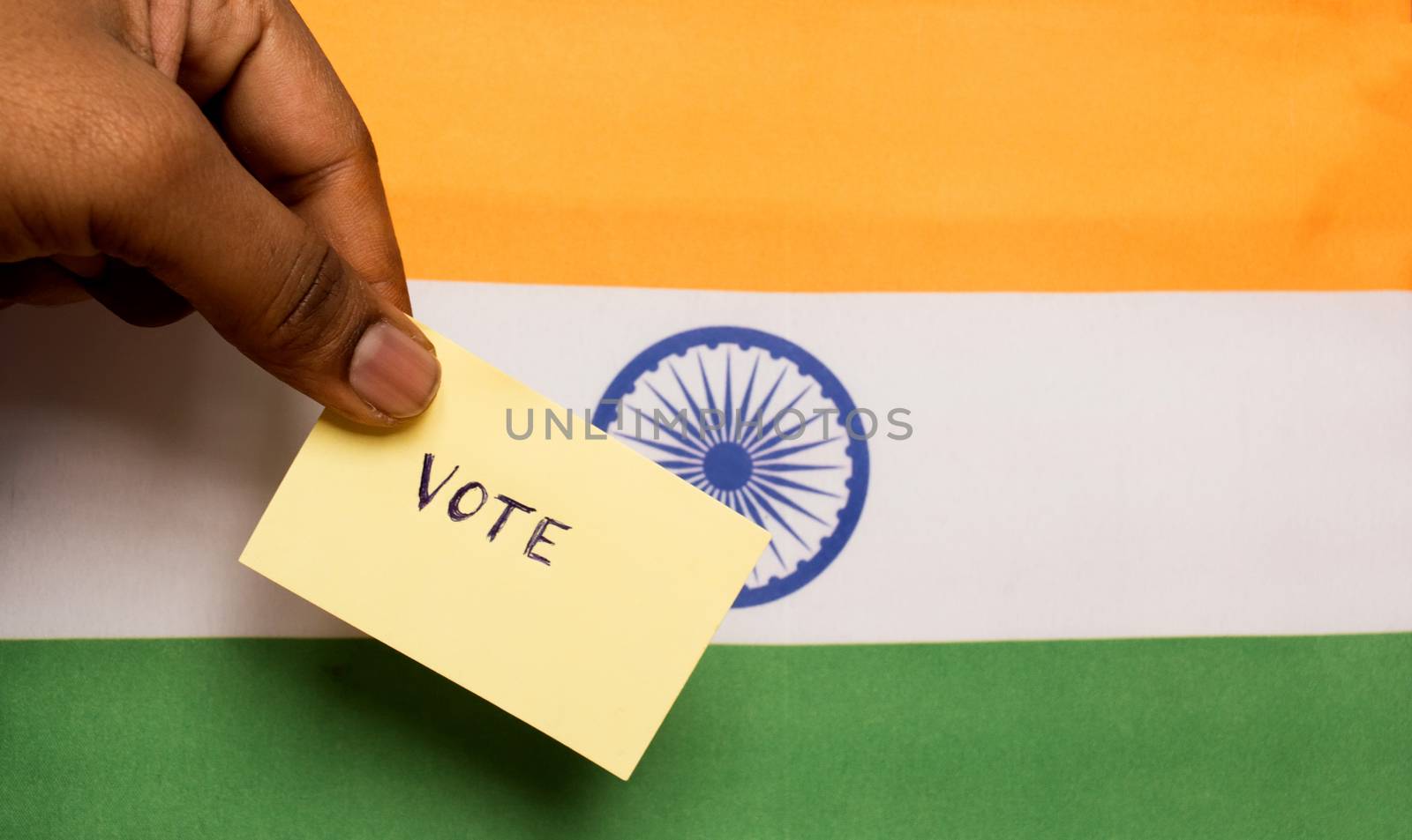 Voting concept - Person holding Hand Written Voting Sticker on India Flag. by lakshmiprasad.maski@gmai.com