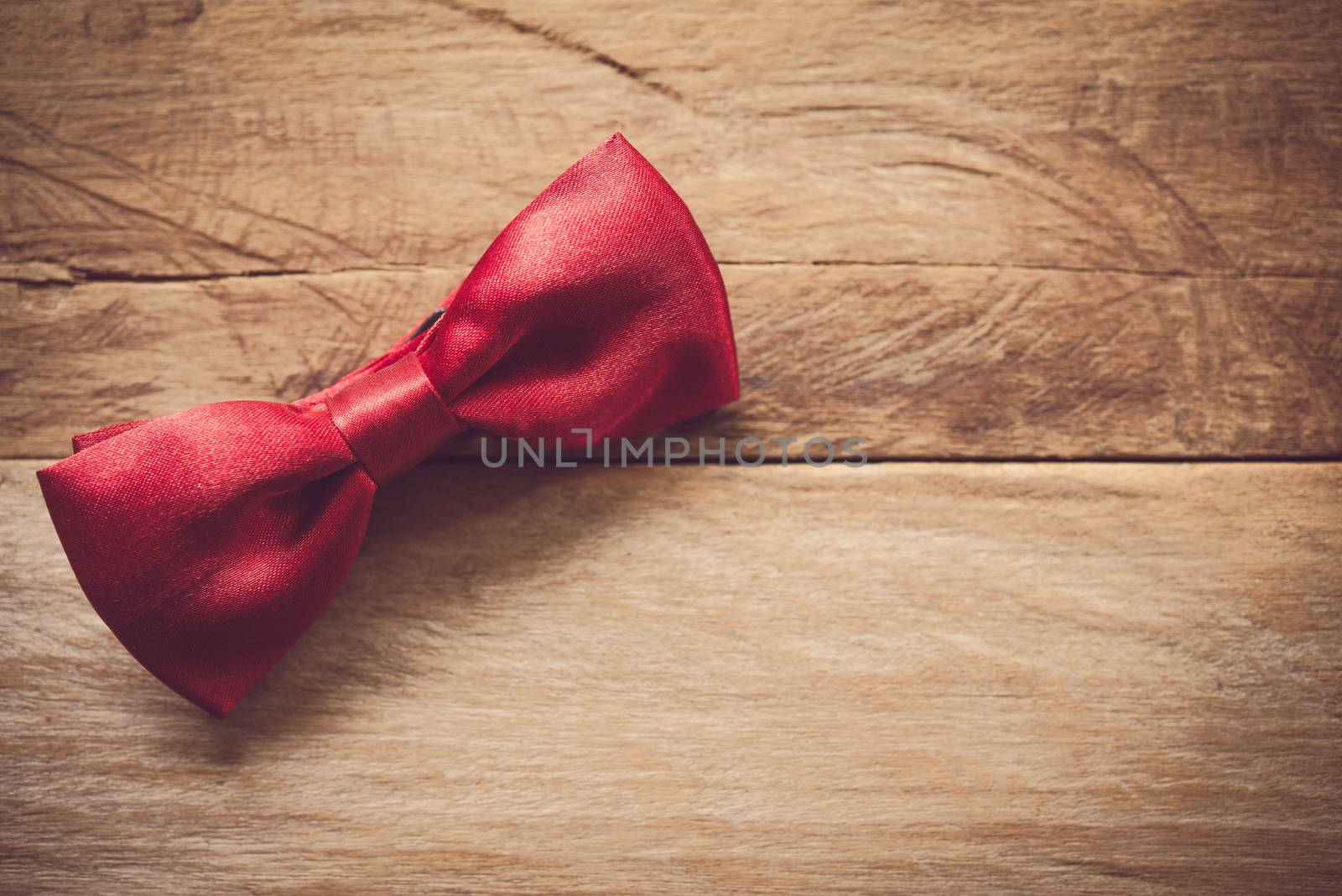 Red bow tie placed on wooden floor.