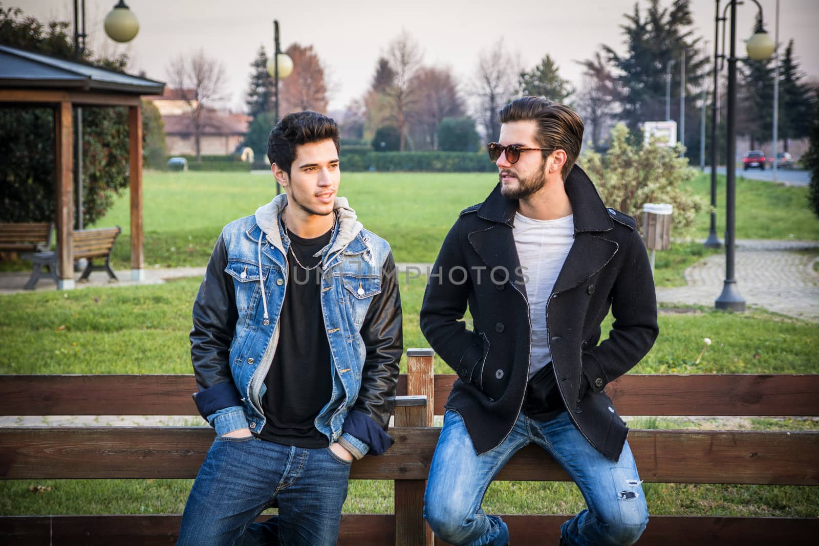 Two handsome casual trendy young men, 2 friends, in an urban park walking and chatting together