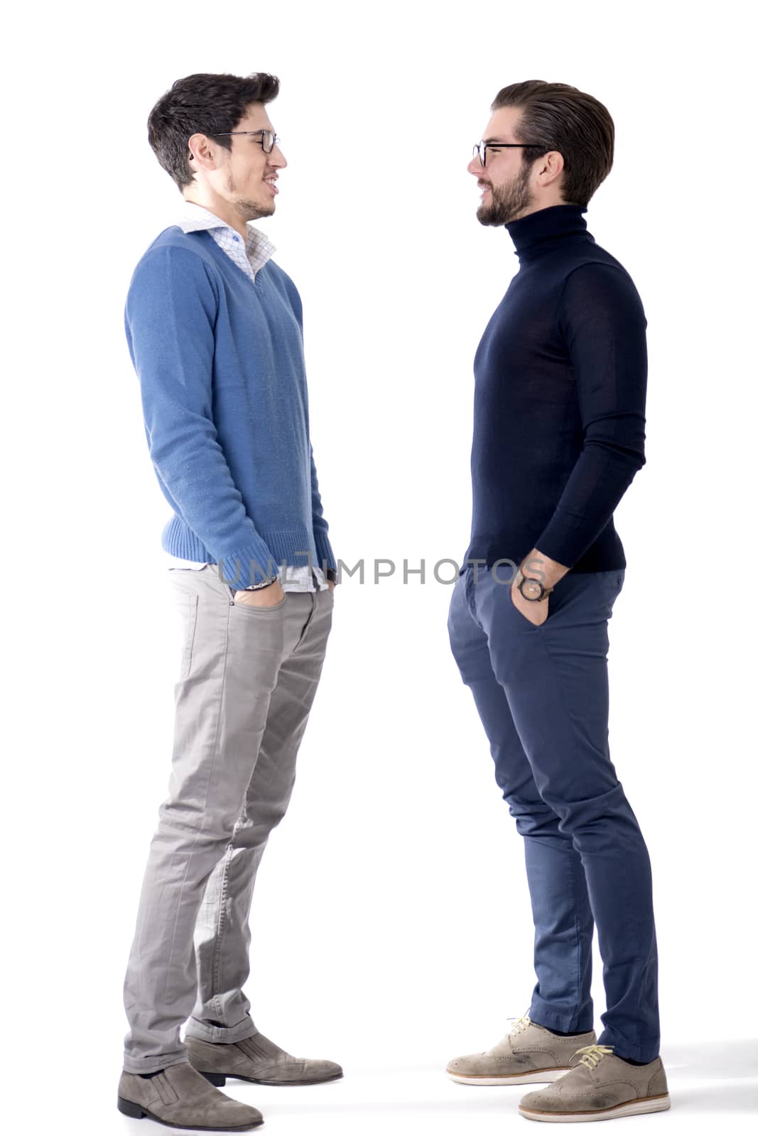 Two good-looking young men with eye-glasses in stylish clothes, looking at one another smiling. Full figure studio shot, isolated on white