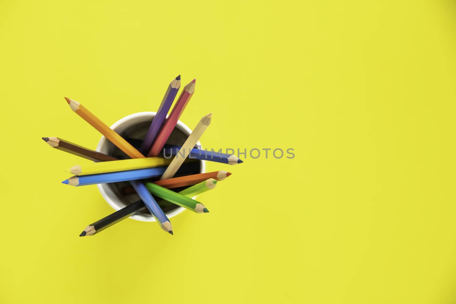 Stack of colored pencils in a glass on yellow background