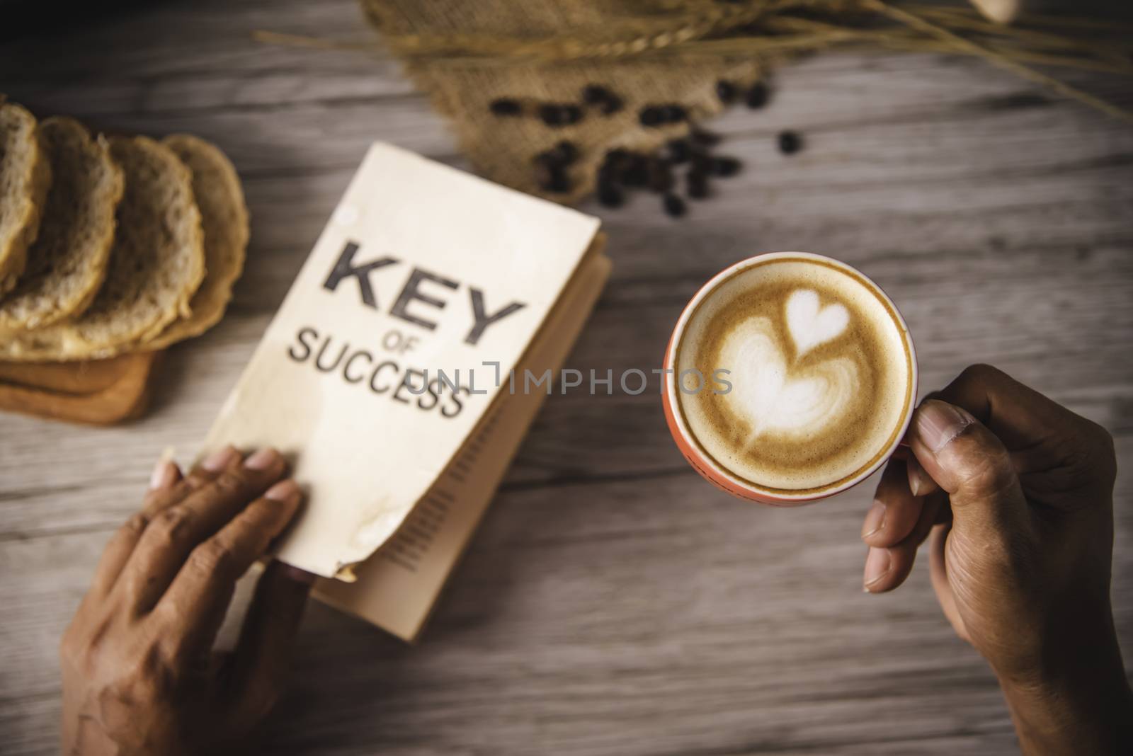 Hand holding a cup of coffee and reading a book key of success - by photobyphotoboy