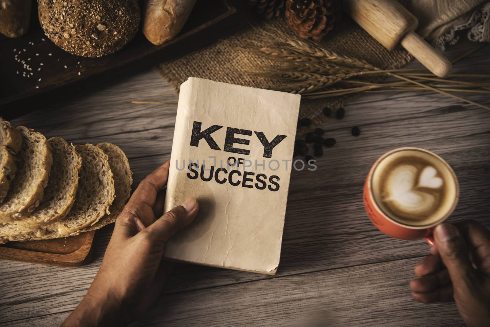 Hand holding a cup of coffee and reading a book key of success - by photobyphotoboy