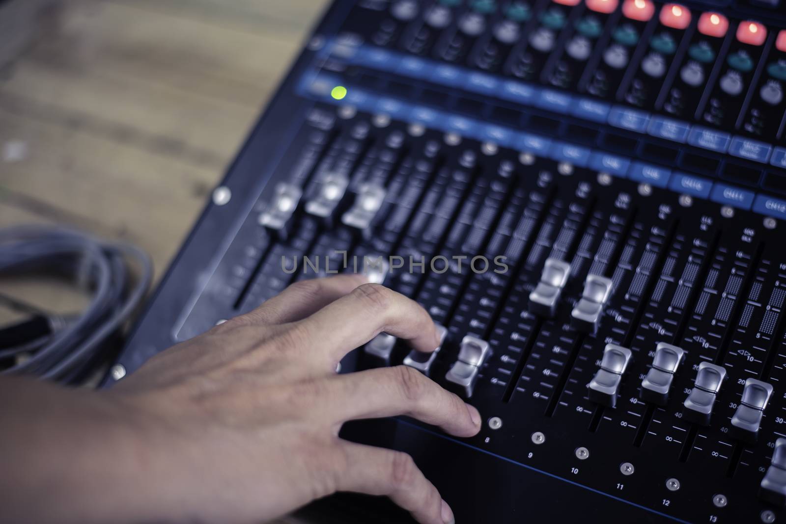 The DJ is adjusting the volume of the sound. Professional audio mixing console
